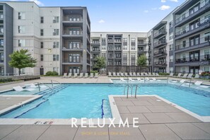 Un moderno edificio de apartamentos con piscina central, sillones de descanso y cielo despejado.