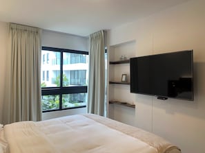 A hotel room with a bed, a television, a window with curtains, and a view of a building outside. - Aparts4Days 1 or 2 Bedroom Apart SanIsidro NearLimaGolf (Lima)
