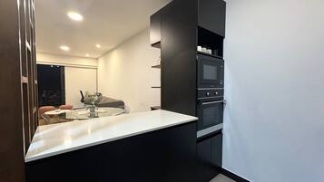 A modern kitchen with a white countertop, black cabinets, a built-in oven, and a microwave.