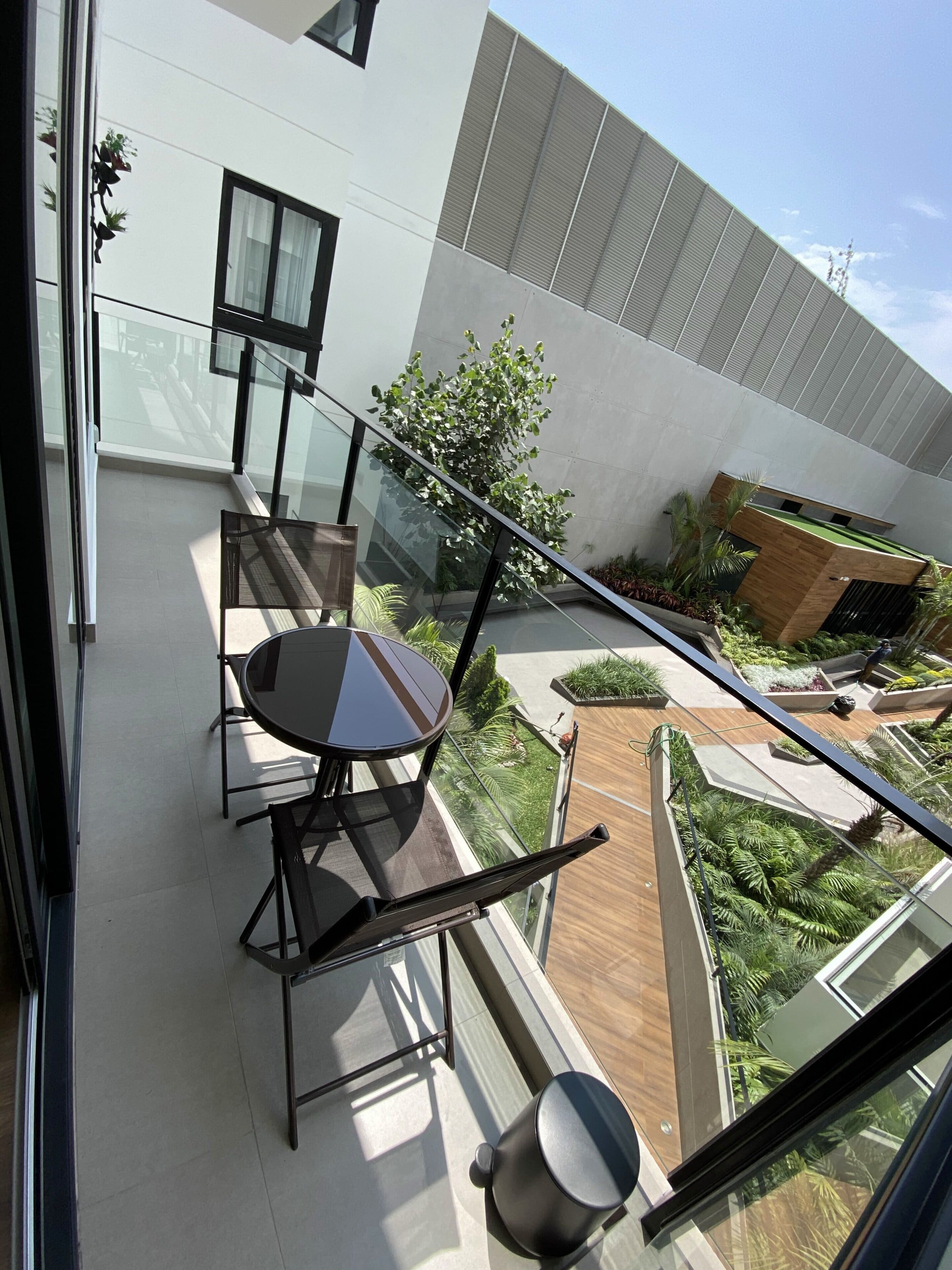 Un balcon moderne avec une balustrade en verre, une table à manger avec des chaises et une vue sur un jardin aménagé.