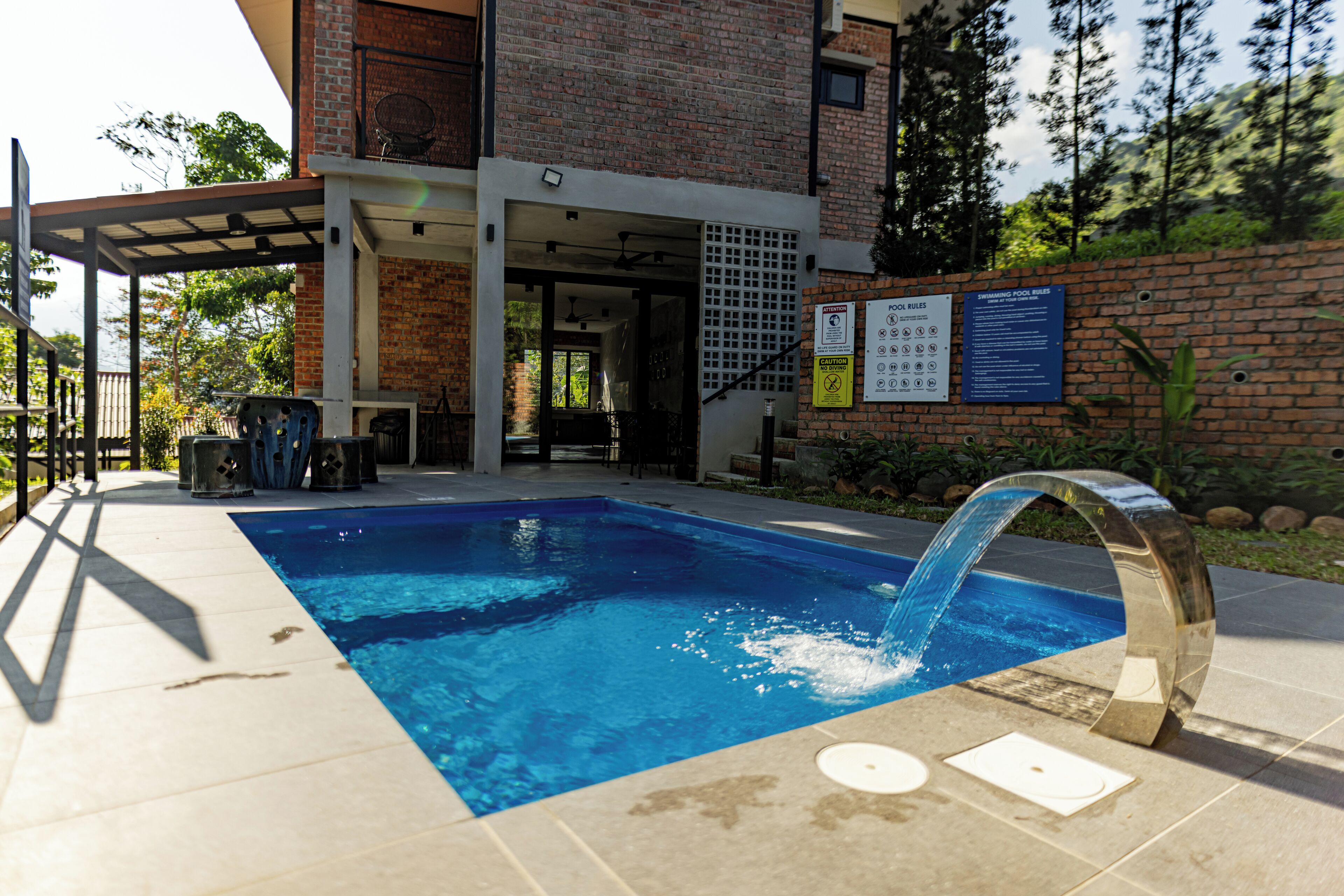 Una piscina con elemento d'acqua, un portico coperto e un edificio in mattoni con posti a sedere all'aperto.