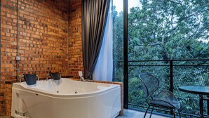A modern bathroom with a large bathtub, a brick wall, and a balcony with a chair and table. - Sebayu Retreat Gopeng (Ipoh)