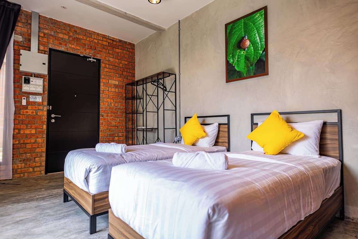 Habitación de hotel con dos camas, un muro de ladrillo, una puerta negra y una obra de arte con una hoja verde en la pared.