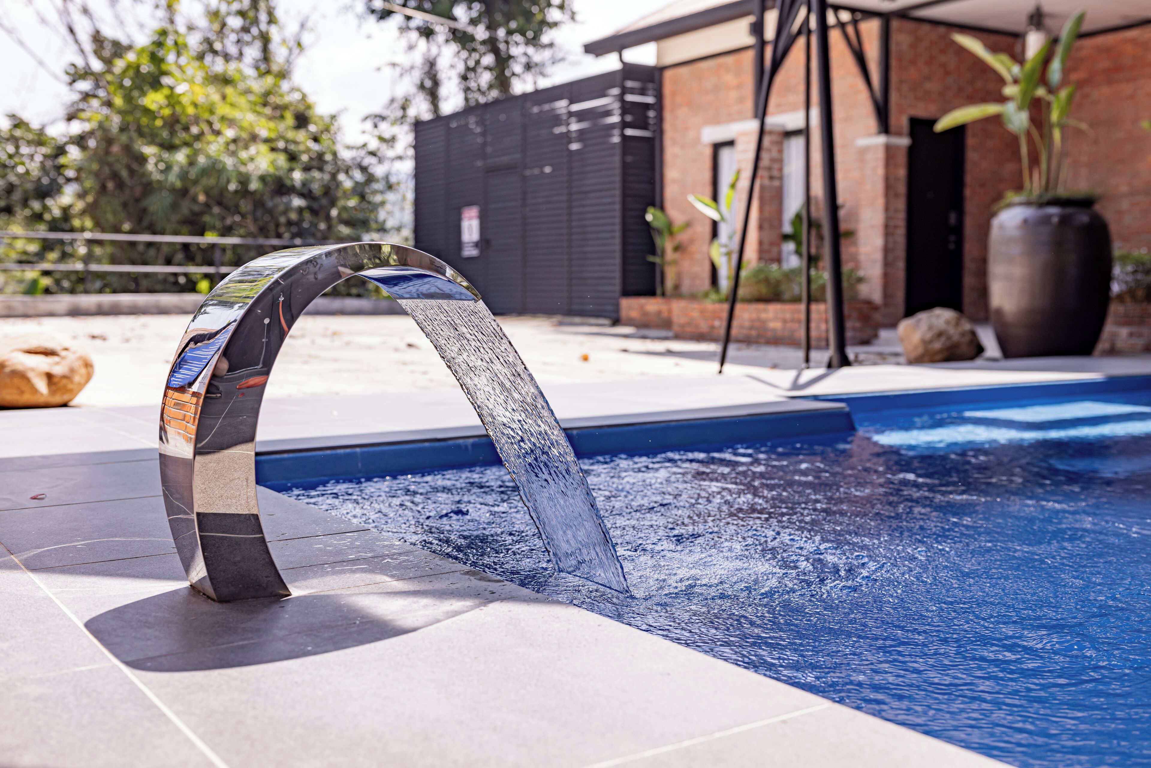 A modern outdoor pool with a unique metal water feature.