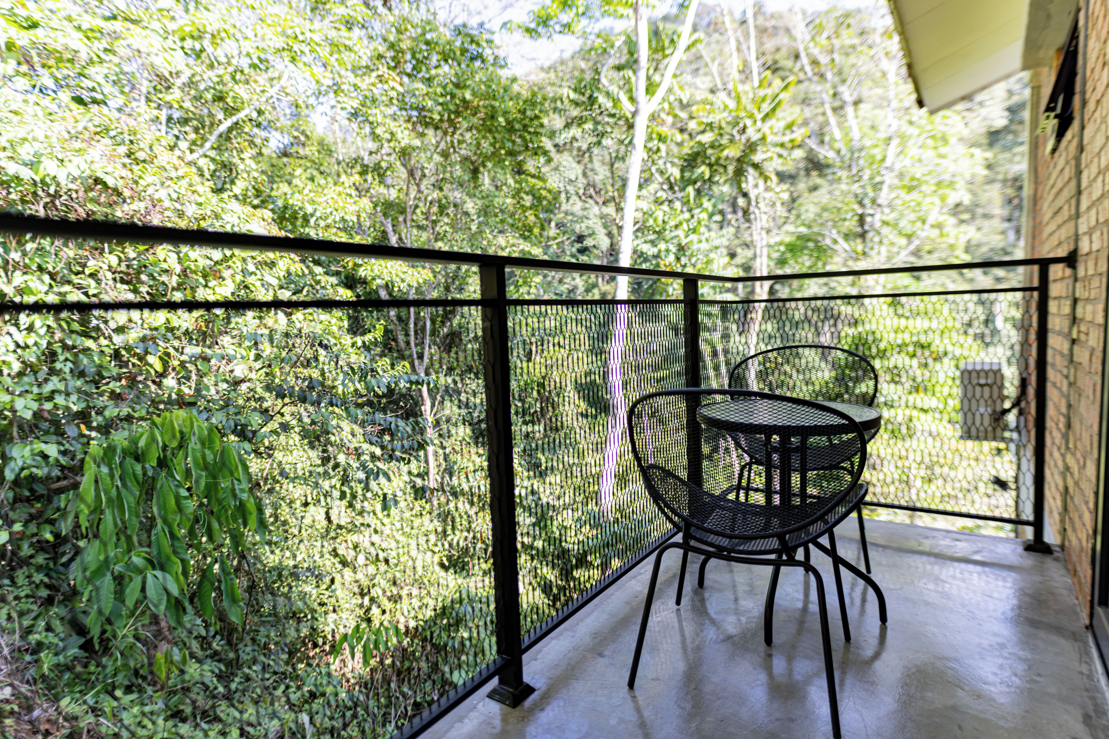 Een balkon met een metalen tafel en stoelen, omgeven door weelderige begroeiing.
