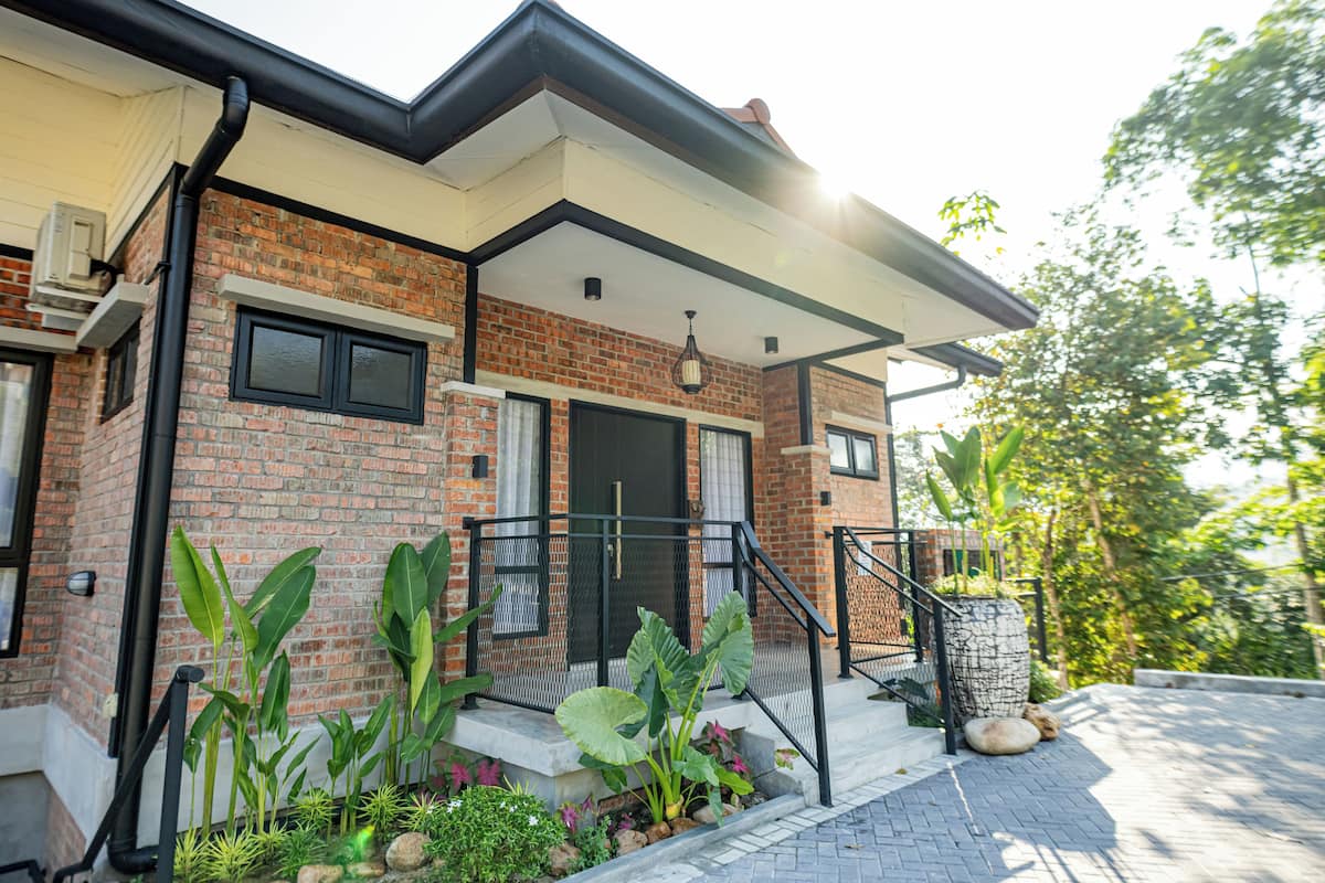 Una casa moderna con fachada de ladrillo, una puerta negra y un pequeño jardín frontal con plantas y un árbol en maceta.