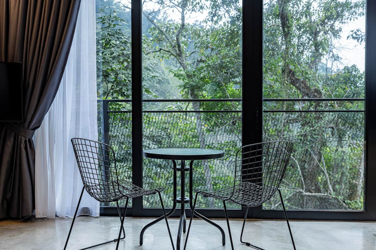 Una habitación con un ventanal grande, dos sillas de alambre y una pequeña mesa redonda.