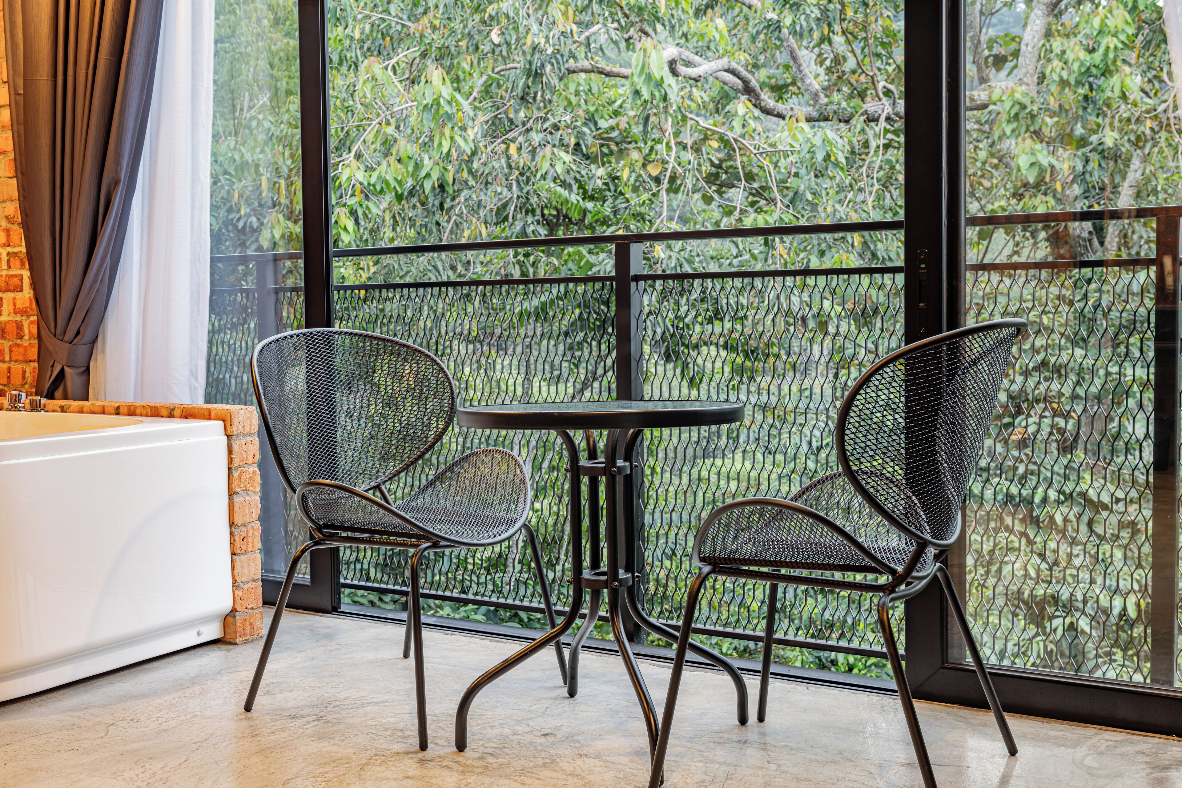 A balcony with two metal chairs and a small table, overlooking a lush garden.