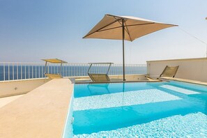 A rooftop pool with clear blue water, sun loungers, and umbrellas.