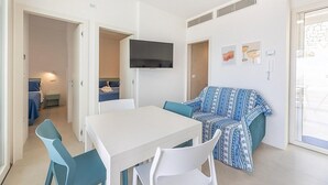 Un espacio habitable compacto con zona de comedor, sofá y televisor montado en la pared.