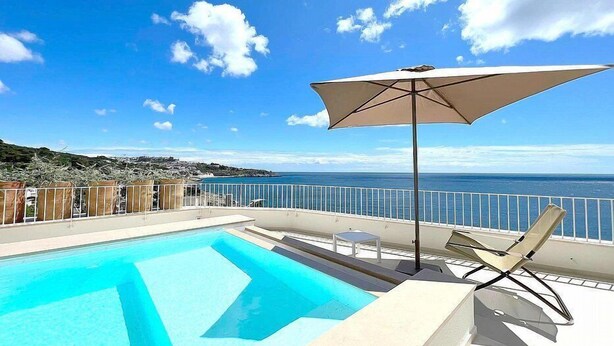 Una piscina con vista despejada al océano y una playa al fondo.