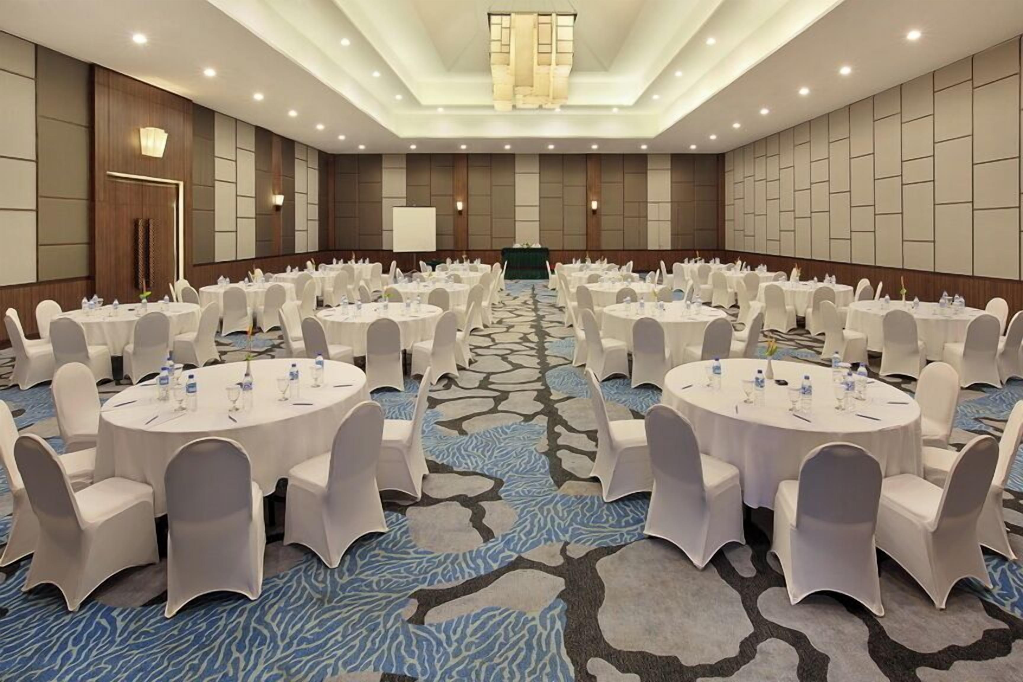 A large conference room with round tables and white chairs, a carpeted floor, and a chandelier.
