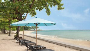 A beach with lounge chairs and a large umbrella. - Manado Tateli Resort and Convention (Pineleng)
