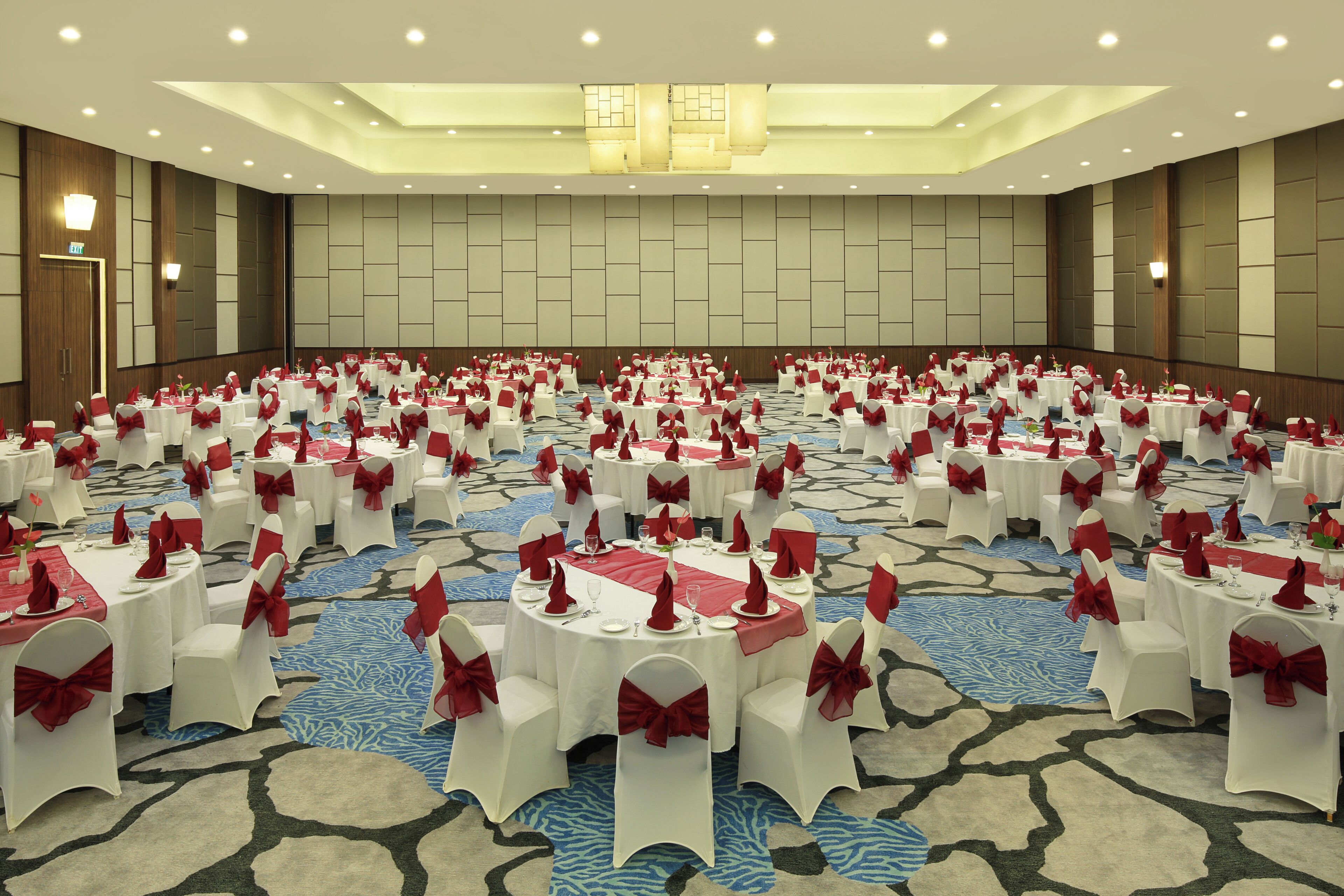 A large conference room with round tables, white chairs, and red sashes.