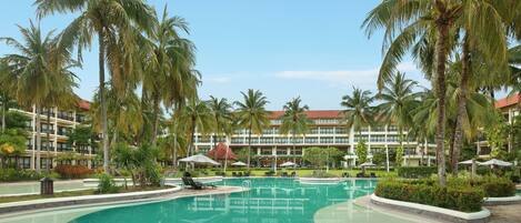 A resort pool with palm trees, a building with a red roof, and a clear blue sky.