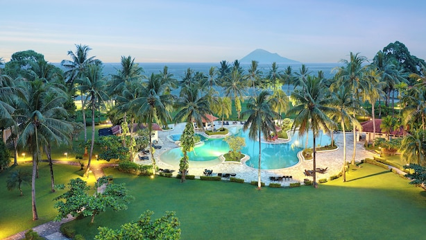 A resort with a large pool surrounded by palm trees and a view of the ocean. - Manado Tateli Resort and Convention (Pineleng)