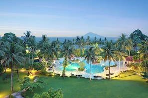 A resort with a large pool surrounded by palm trees and a view of the ocean. - Manado Tateli Resort and Convention (Pineleng)