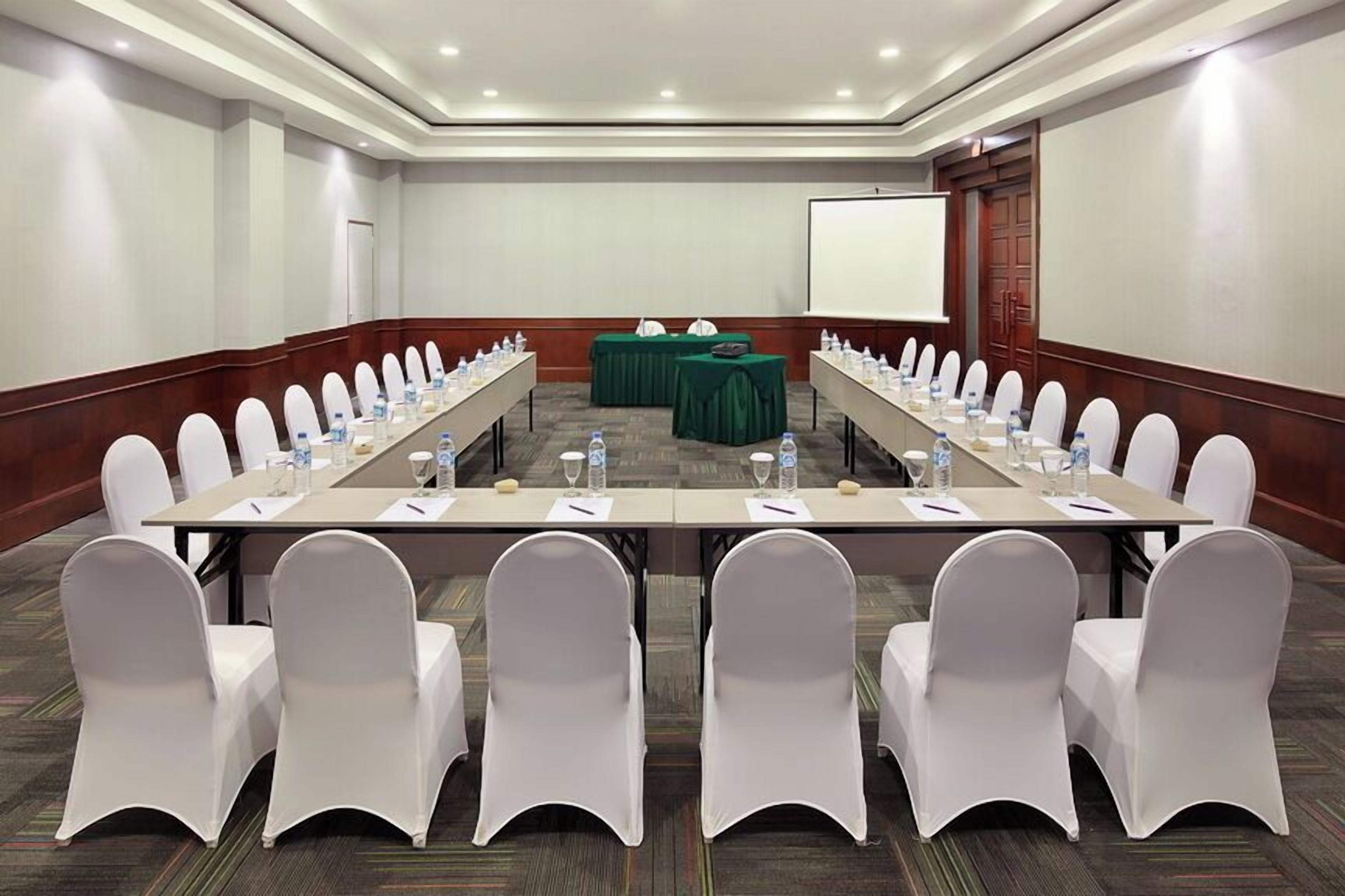 A conference room with a long table, white chairs, and a projector screen.