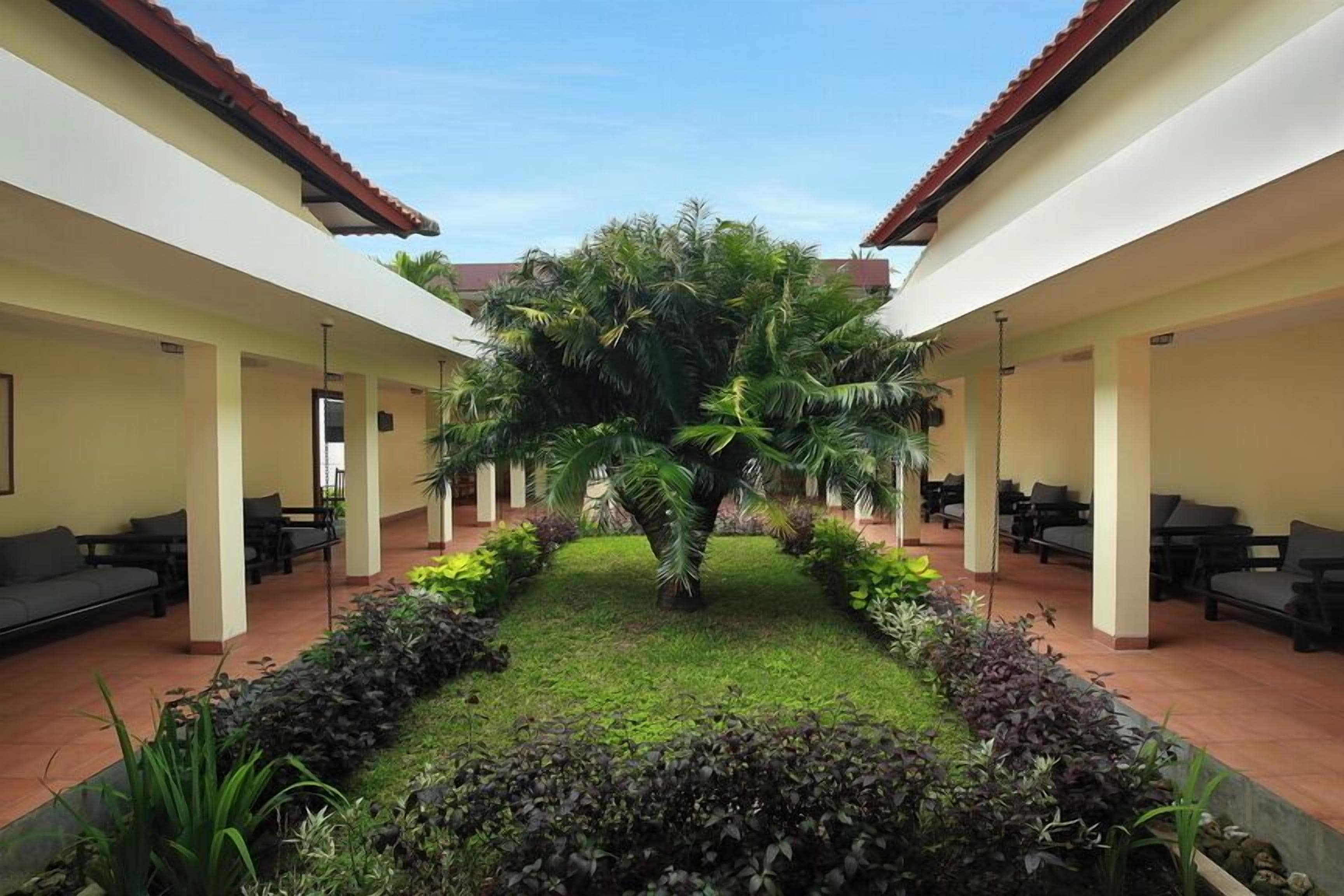 A courtyard with a central palm tree, surrounded by seating areas and a well-maintained garden.