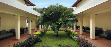 Un patio con una palmera en el centro, rodeado de zonas de estar y un jardín bien cuidado.