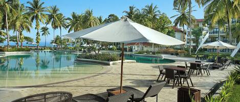A poolside area with lounge chairs, umbrellas, and a view of the pool and palm trees.
