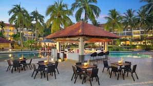 A resort pool area with outdoor seating and a bar, surrounded by palm trees and hotel buildings. - Manado Tateli Resort and Convention (Pineleng)