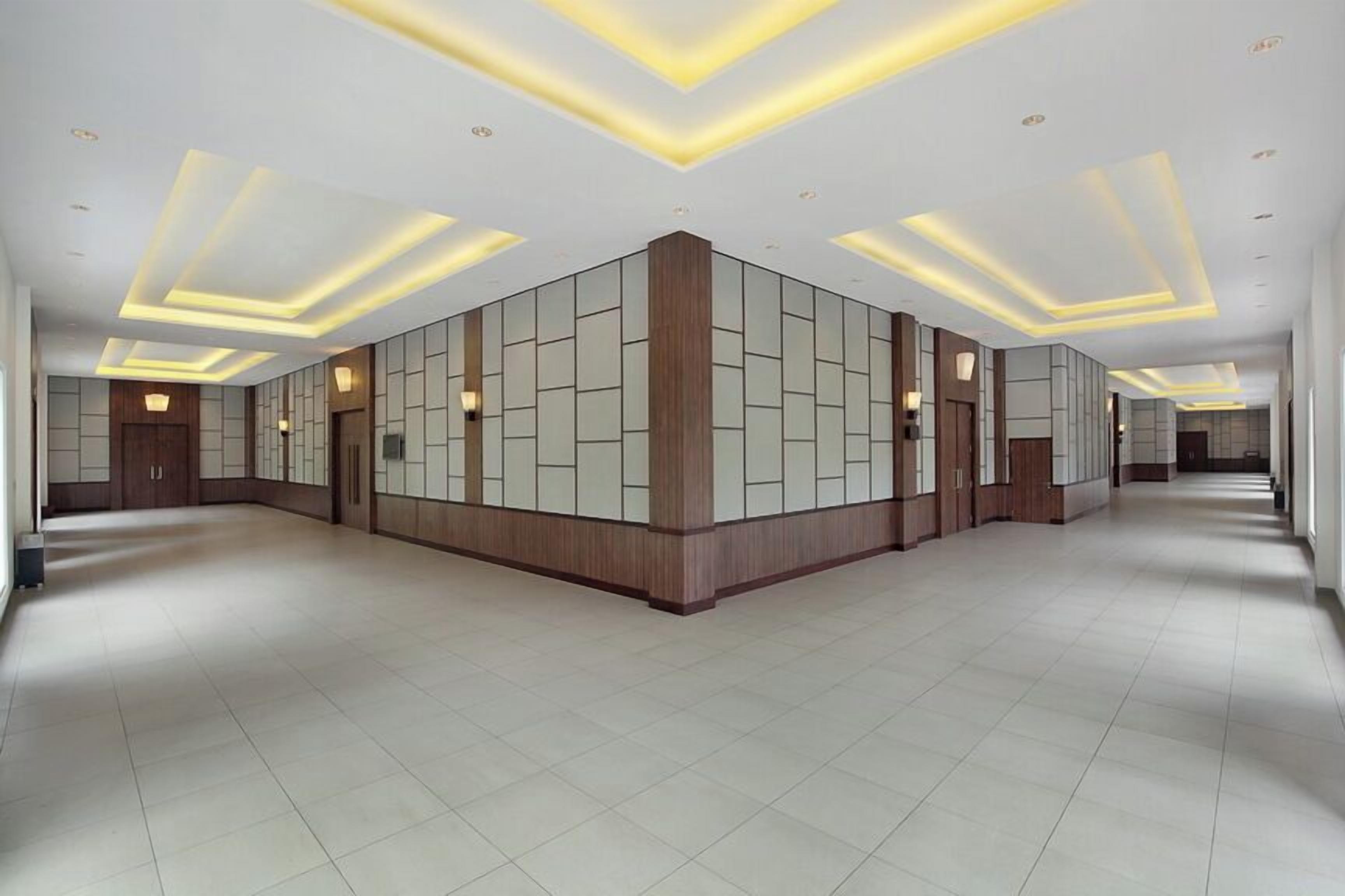 A spacious hotel lobby with a modern design, featuring a central column, recessed lighting, and a tiled floor.