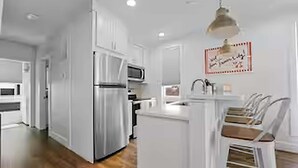 A modern kitchen with white cabinetry, a stainless steel refrigerator, and a built-in oven. - West Bay Hideaway | Rooftop Condo Near Beach/DT TC (Traverse City)