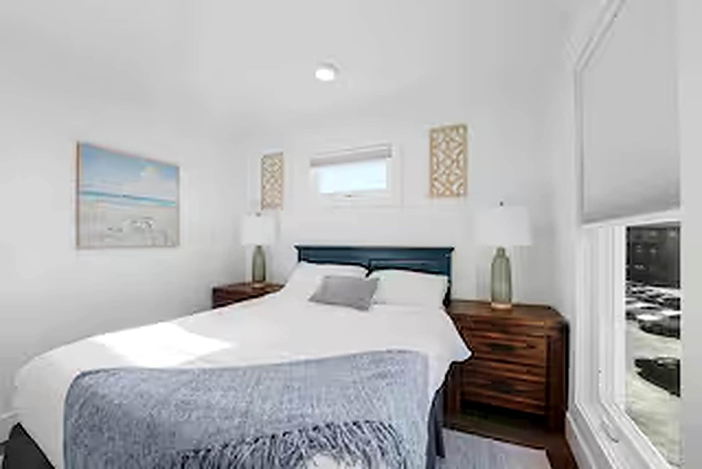 Une chambre à coucher avec un lit, des tables de chevet, une fenêtre et des œuvres d’art accrochées aux murs.