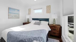 A bedroom with a bed, bedside tables, a window, and artwork on the walls. - West Bay Hideaway | Rooftop Condo Near Beach/DT TC (Traverse City)