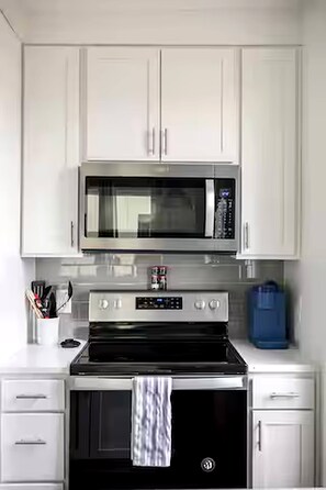 A kitchen with white cabinets, a stainless steel microwave, a black oven, and a blue water dispenser.