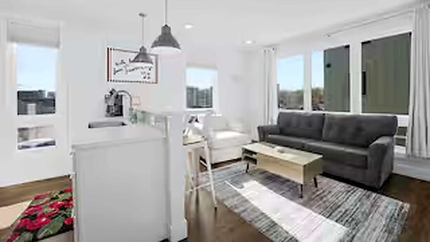 A modern living room with a grey sofa, a coffee table, and a dining area with a white table and chairs. - West Bay Hideaway | Rooftop Condo Near Beach/DT TC (Traverse City)