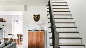 A staircase with wooden steps and a metal handrail, a wooden cabinet with a vase and a book, and a grey sofa in a modern interior. - Woodland Chase - Pool + Hot Tub by Wineries (Prince Edward)