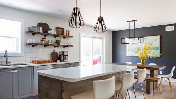 A modern kitchen with a central island, bar stools, pendant lights, and a dining area with a table and chairs. - Woodland Chase - Pool + Hot Tub by Wineries (Prince Edward)