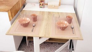 A small dining table with pink placemats, two white stools, and a framed picture on the wall.