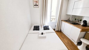 A small, modern room with a bed, a kitchenette, and a window with curtains.