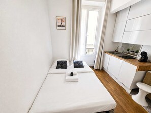 A small, modern room with a bed, a kitchenette, and a window with curtains. - Studio equipe centre nation - Paris 12 - 2P (Paris)