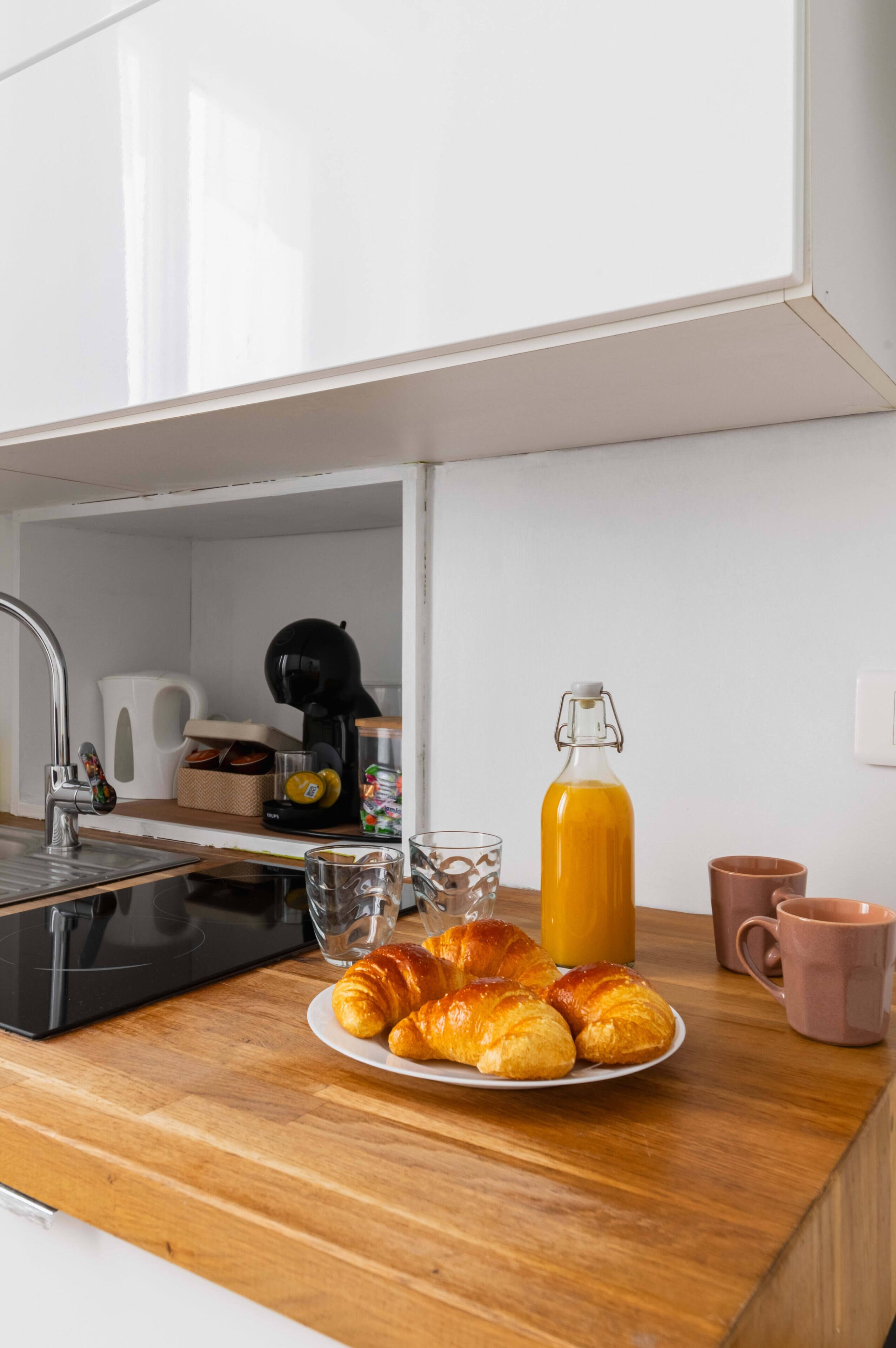 A kitchen counter with croissants, a glass of orange juice, and a coffee maker.