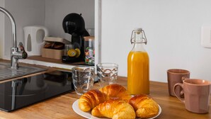 A kitchen counter with croissants, a glass of orange juice, and a coffee maker.