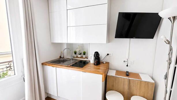 A compact kitchenette with a sink, countertop, and a TV mounted above.