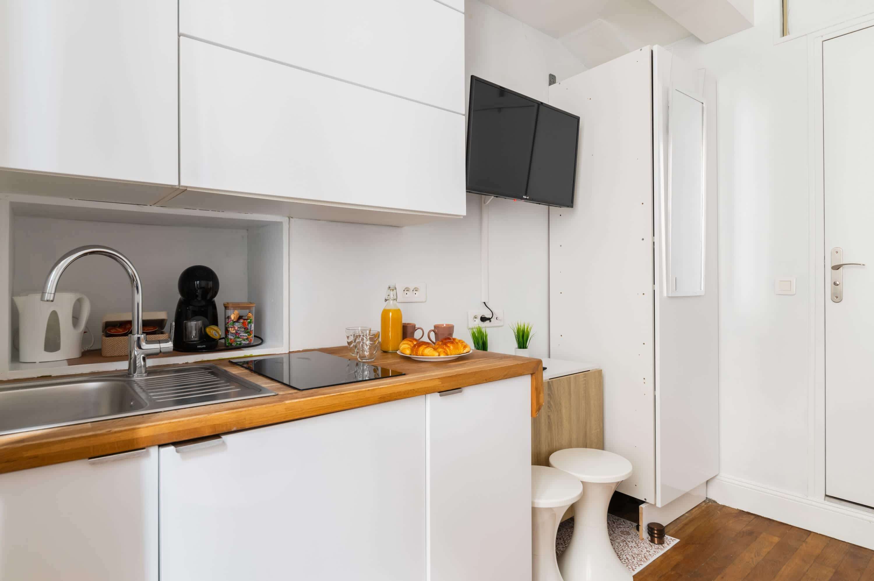 A modern kitchen with white cabinetry, a wooden countertop, a built-in sink, and a coffee maker.
