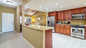 A kitchen with wooden cabinets, stainless steel appliances, a granite countertop, and a ceiling fan. - Country Club Experience (Palm Desert)
