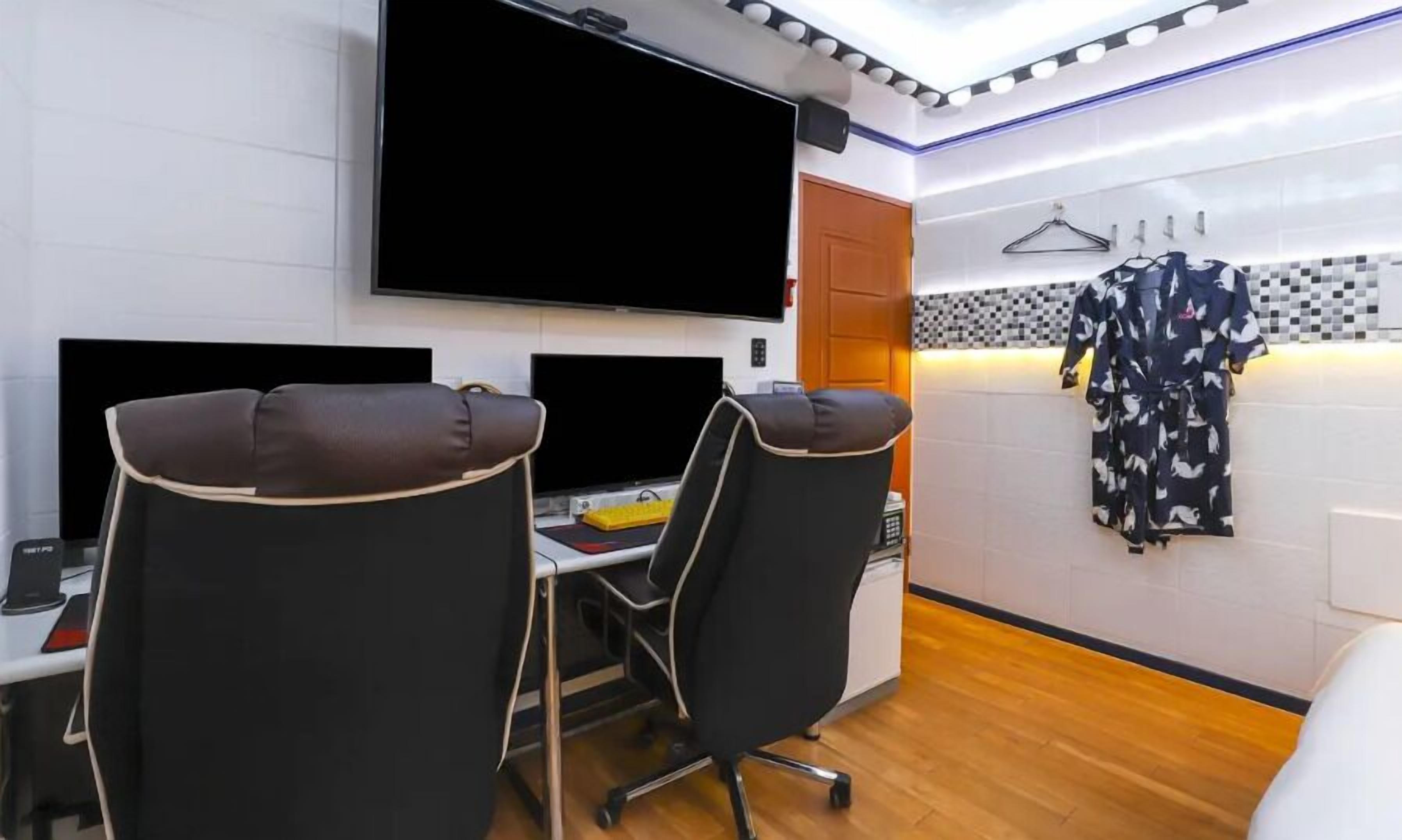A modern room with two black office chairs, a desk with a computer, a flat-screen TV mounted on the wall, and a wardrobe with a checkered pattern.