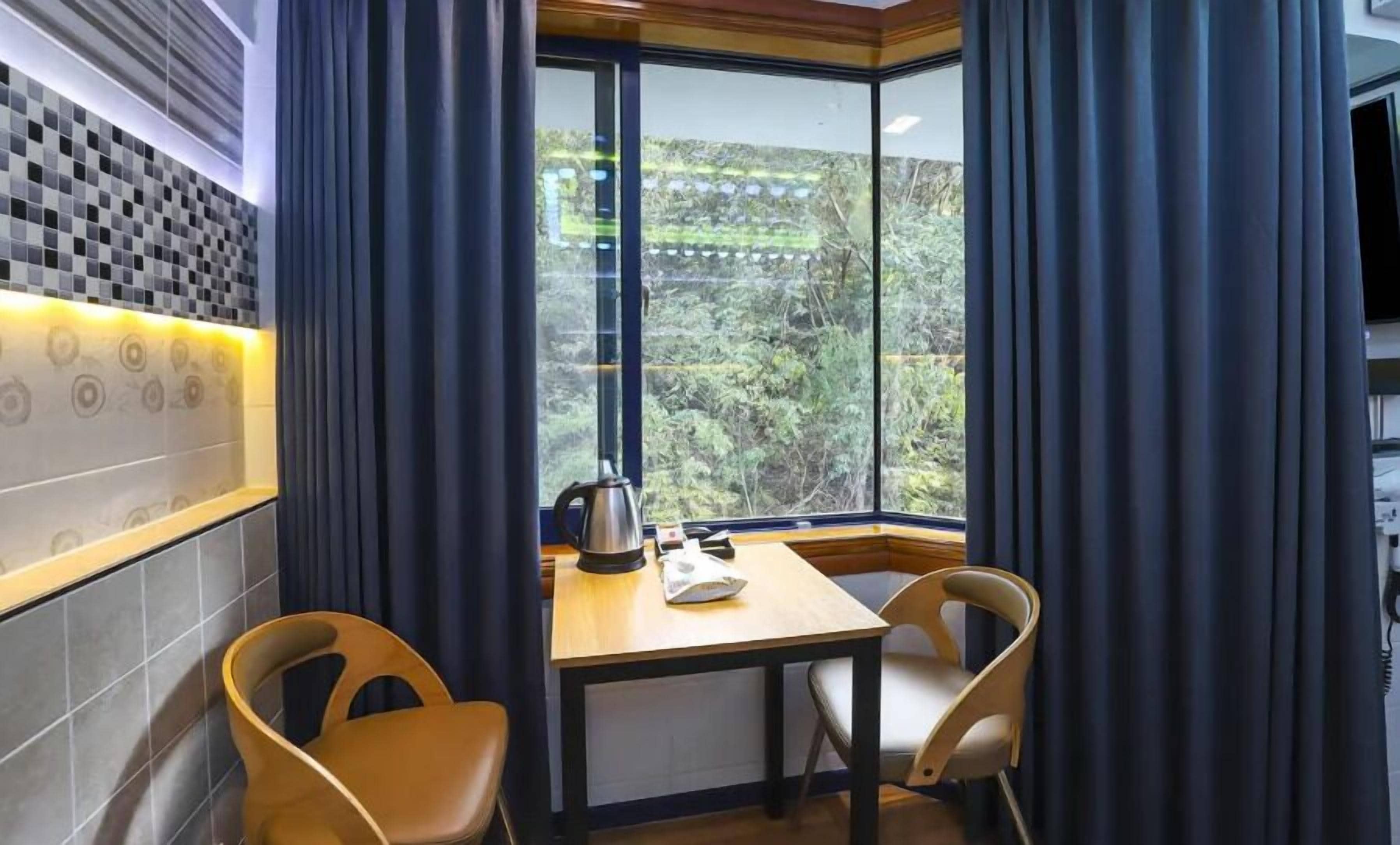 A corner room with a large window, a table, two chairs, and a kettle on the table.