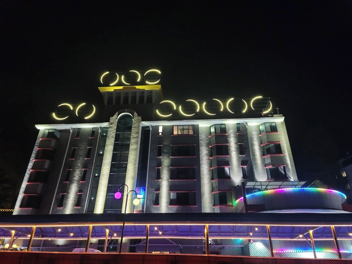 A modern building with illuminated circular patterns on the roof and a multi-story structure with balconies.