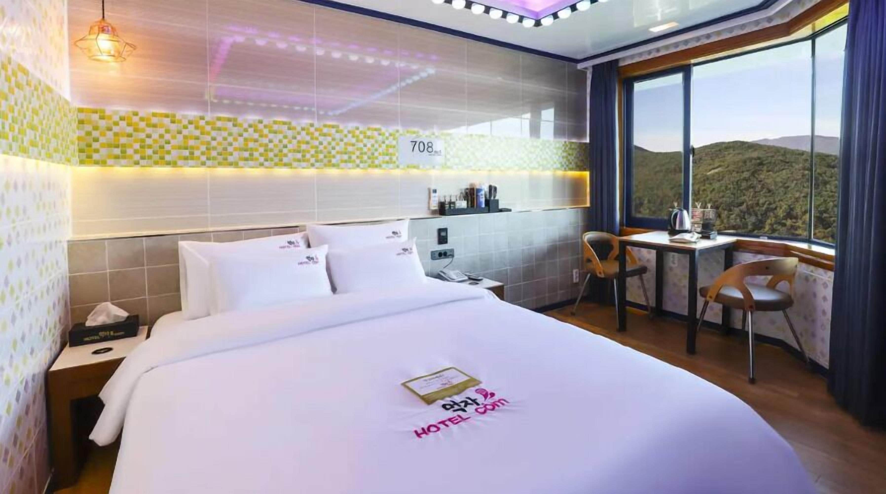 Habitación de hotel con una cama grande, un escritorio y una silla. Se ve una ventana con vistas a las colinas.
