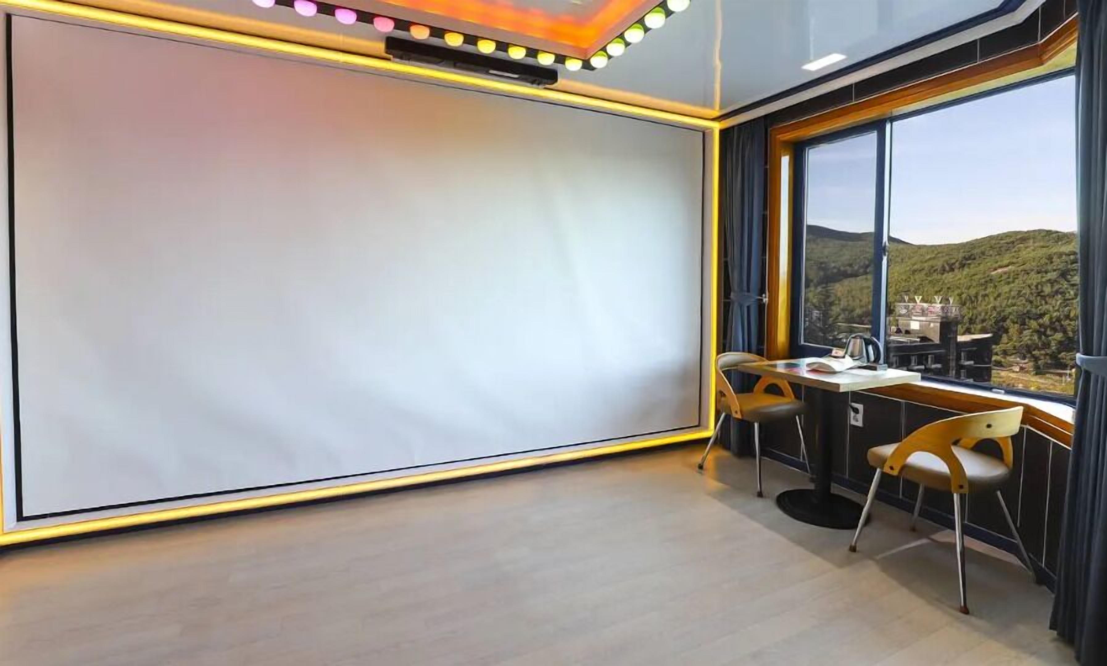 A modern room with a large whiteboard, a desk with two chairs, and a view of a mountainous landscape through large windows.