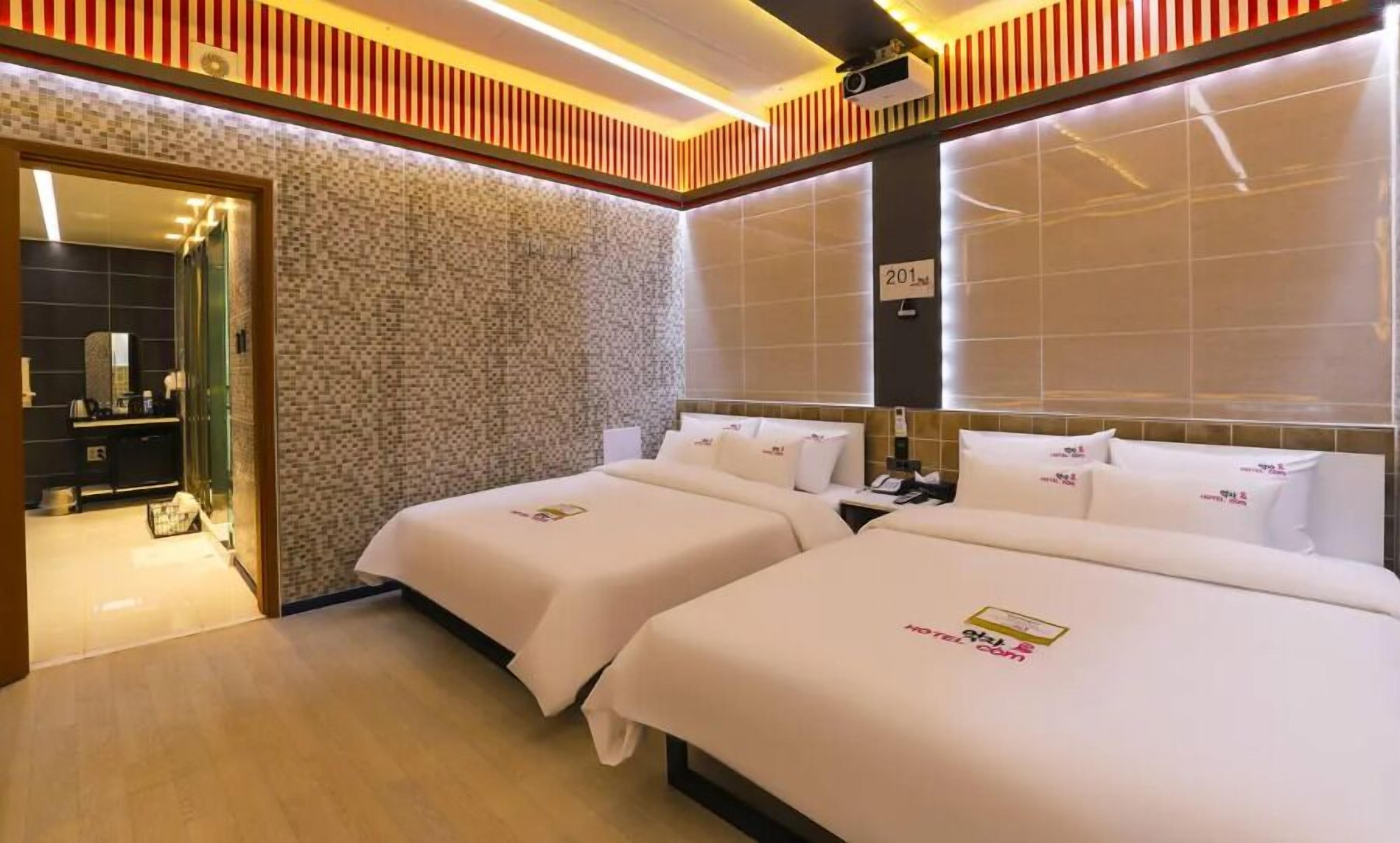 A hotel room with two beds, a bathroom with a mirror, and a wall with a textured pattern.