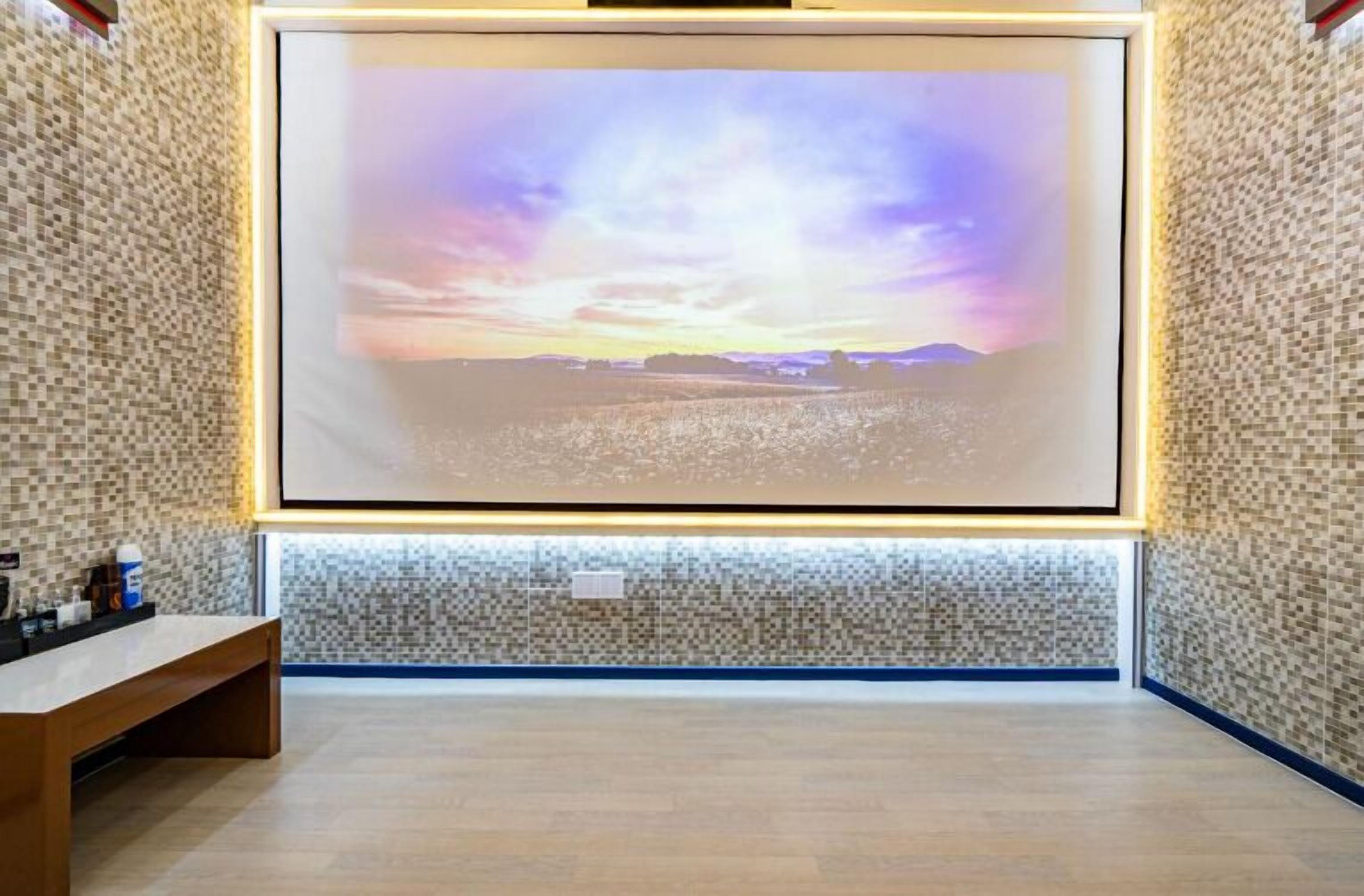 A room with a large framed picture of a sunset over a body of water, a wooden bench, and a tiled wall.
