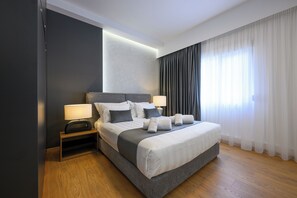 Et moderne hotelværelse med en stor seng, sengeborde, lamper og udsigt til det fri gennem lette gardiner.